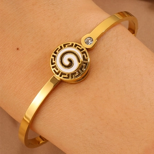 Detail of gold-plated bangle with white enamel spiral and Greek key pattern on wrist