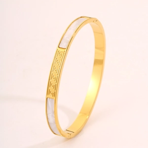 Detail of gold stainless steel bangle with Greek key pattern and white shell inlays