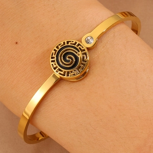 Macro shot of gold stainless steel cuff featuring a Greek key pattern and spiral design