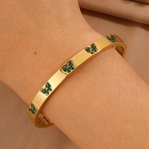 Close-up van een gouden vlinderarmband met groene zirkonen om een vrouwenpols