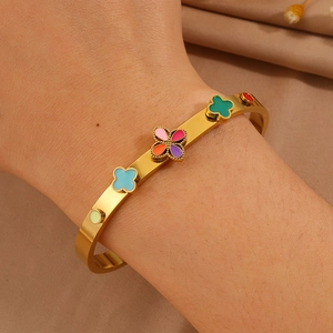 Détail d'un bracelet doré en émail avec trèfles colorés porté au poignet d'un mannequin