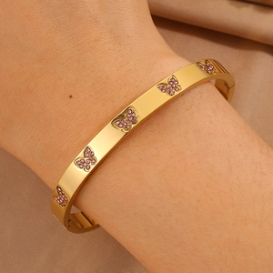 Detail van een gouden vlinderarmband met roze kristallen om de pols, zachte warme achtergrond