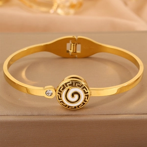 Detailed macro view of gold-tone open bangle with Greek key pattern and white spiral inlay