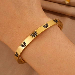 Detail van gouden roestvrijstalen armband met zwarte vlinders en fonkelende kristallen