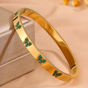Detail van een goudkleurige roestvrijstalen armband met vijf smaragdgroene vlinderpatronen