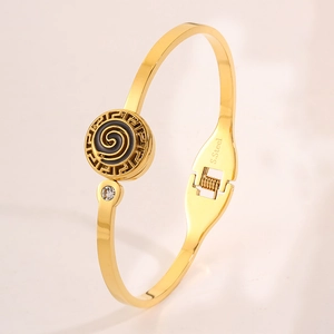 Detailed view of golden stainless steel bracelet with Greek meander and black enamel spiral