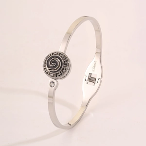Close-up of silver stainless steel bangle featuring black spiral and Greek key patterns