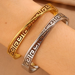 Close-up of gold and silver open bracelets with geometric Greek key patterns on model