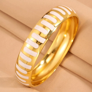 Detail of wide gold stainless steel bangle with white enamel stripes on beige silk
