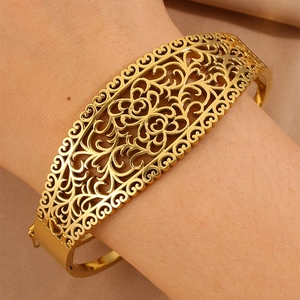 Dettaglio di motivi a cuore traforati su un ampio bracciale rigido in acciaio al titanio dorato