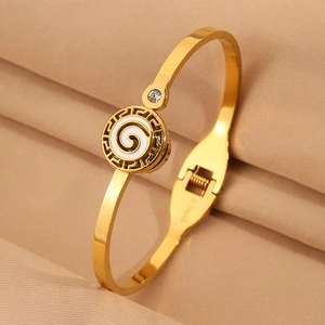 Detailed close-up of golden stainless steel bangle featuring Greek key pattern and white enamel