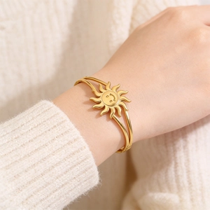 Detail of golden sun smiley face open bangle worn over a cozy cream knit sweater