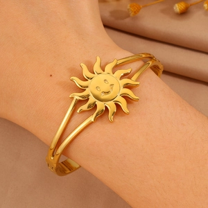 Detail of a gold sun face bangle with dual-track band on a model wrist with satin background
