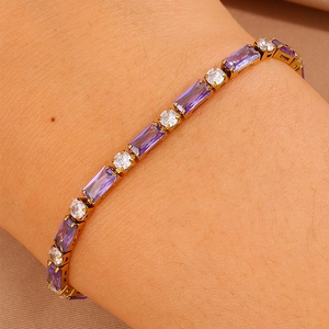 Dettaglio di un bracciale tennis dorato con zirconi viola e bianchi alternati