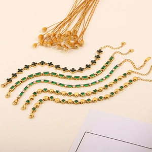 Detailed macro view of five gold-plated bracelets featuring emerald green crystals and charms