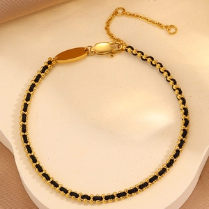 Detail of gold beads and black braided rope bracelet with lobster clasp and charm