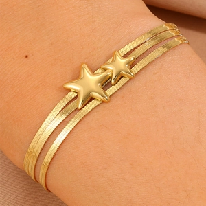 Détail d'un bracelet doré à double chaîne serpent orné de charms étoiles polies sur poignet
