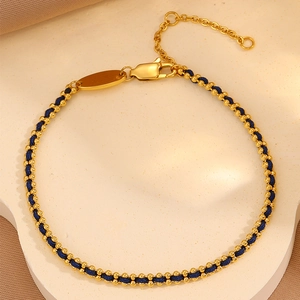 Macro detail of gold plated stainless steel beads woven into a deep blue cord bracelet
