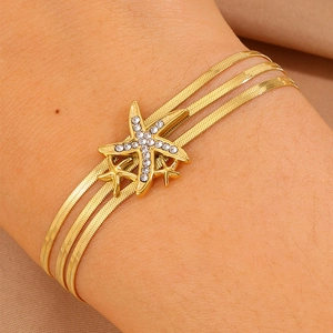 Détail d'un bracelet triple chaîne serpent dorée avec des breloques étoiles de mer