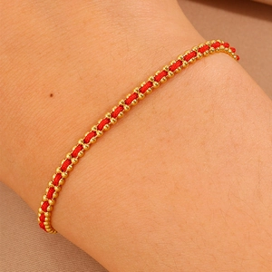 Detail of red woven cord bracelet with gold beads worn on wrist with micro texture