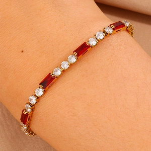 Primo piano di un bracciale tennis placcato oro con pietre rosse e zirconi sul polso