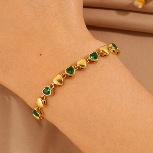 Detail of gold-plated heart chain bracelet with green heart-shaped gemstones on wrist