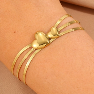 Détail d'un bracelet triple chaîne serpent dorée avec pendentifs coeurs sur le poignet
