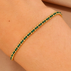 Close-up of handmade gold bead and green braided cord bracelet on a woman's wrist