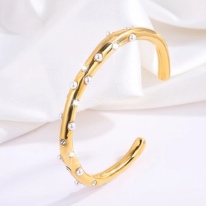 Detailopname van gouden C-vormige titanium armband met parels en zirkonia kristallen