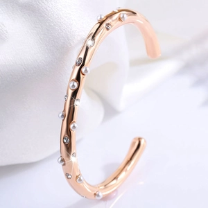 Detail van een roségouden C-vormige armband met microparels en fonkelende strassteentjes