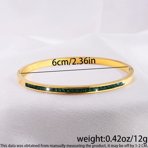Primer plano de un brazalete de acero inoxidable dorado con piedras rectangulares verde esmeralda