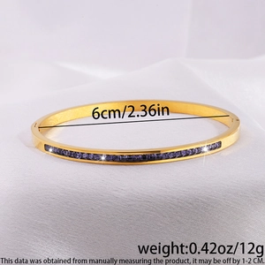 Detalle de brazalete de acero dorado con piedras cuadradas moradas sobre seda blanca