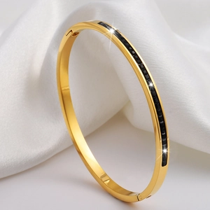 Detalle de brazalete dorado de acero inoxidable con piedras negras cuadradas en seda
