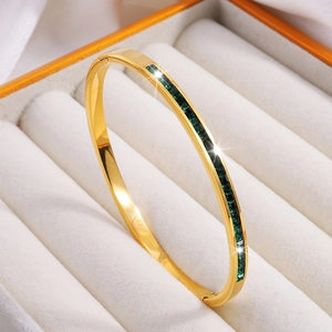 Detalle de un brazalete de acero de titanio dorado con cristales verdes cuadrados en caja