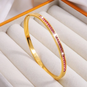 Detalle de brazalete de acero de titanio dorado con circonitas cuadradas rosas