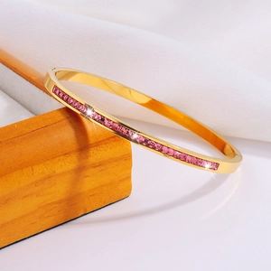 Primer plano detallado del brazalete de acero dorado con cristales cuadrados de color rosa
