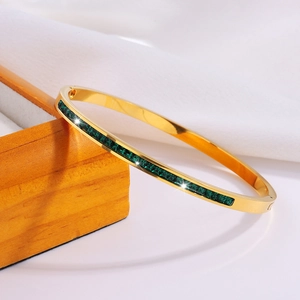Detalle del brazalete de acero dorado con cristales cuadrados verde esmeralda sobre madera