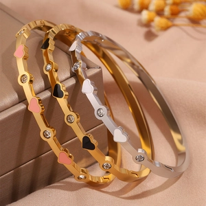 Dettaglio di tre bracciali a cuore in titanio con cristalli su sfondo di seta rosa