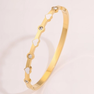 Dettaglio del bracciale dorato in acciaio al titanio con cuori bianchi e zirconi tondi