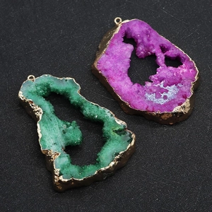 Détail de pendentifs en quartz druzy violet et vert avec bords dorés sur fond noir texturé