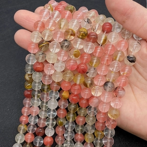 Detail of natural strawberry quartz and rutilated quartz round beads held in palm
