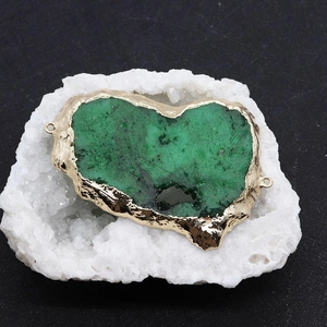 Détail d'un pendentif en cristal naturel vert avec placage d'or sur socle en cristal blanc