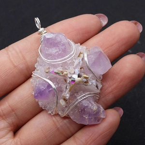 Close-up of handmade raw amethyst stone cross pendant wrapped in silver wire held in hand