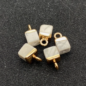 Detalle macro de colgantes de piedra imperial en forma de cubo con enganches de metal dorado