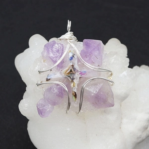 Natural raw amethyst stone cross wire wrapped pendant displayed on a white crystal cluster