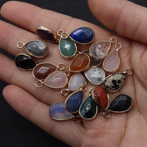 Vue détaillée de pendentifs goutte en pierre naturelle dorés tenus à la main