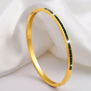 Elegante brazalete bañado en oro con circonitas verdes sobre fondo de seda blanca pura