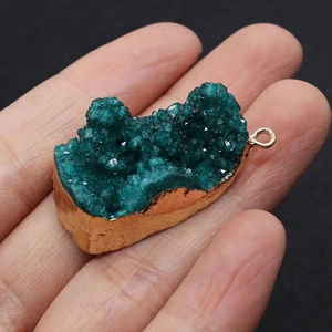 Détail macro d'un pendentif en cristal druzy vert naturel avec bordure dorée tenu à la main