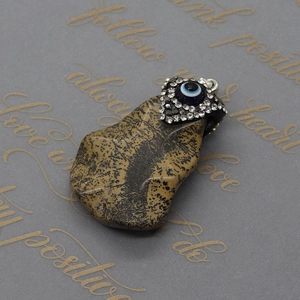 Macro detail of natural stone pendant with evil eye charm and inlaid rhinestones