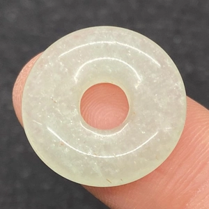 Close-up of green aventurine stone donut pendant held between fingers showing natural texture